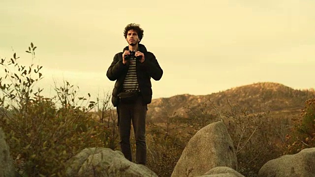 一个25岁的年轻人，旅行潮人，在约塞米蒂国家公园魔鬼舞池附近用双筒望远镜观察大自然视频下载