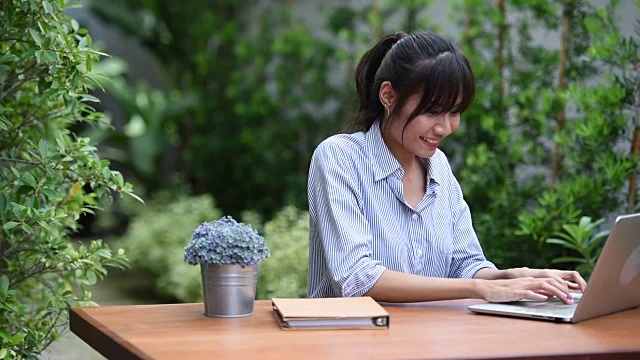 亚洲年轻女子坐在工作场所，在花园里使用笔记本电脑视频素材