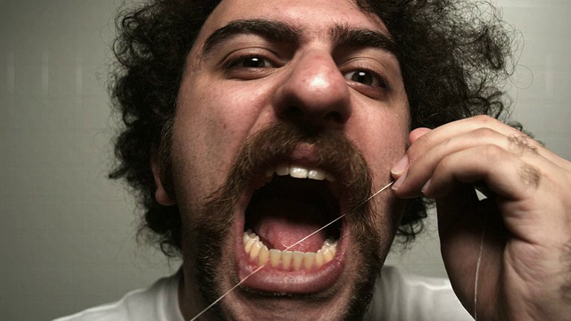 乔治亚州亚特兰大，一名年轻男子看着镜头，用牙线使劲清洁牙齿视频素材
