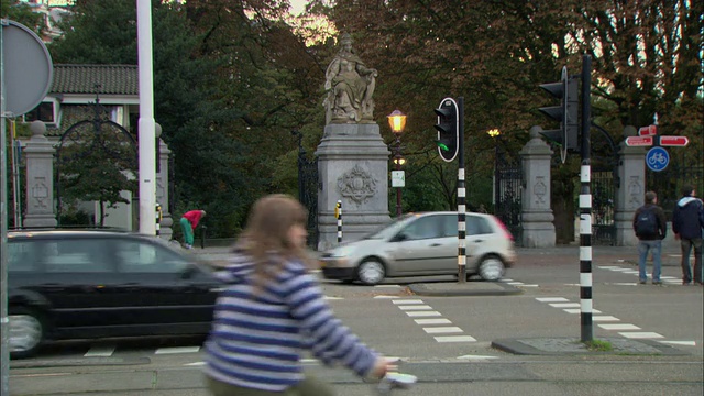 T/L WS骑自行车的人和行人穿过繁忙的十字路口，雕塑在入口处的公园在背景/荷兰阿姆斯特丹视频素材