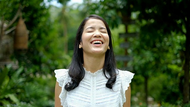快乐年轻的亚洲妇女在白色西装微笑和笑对绿色的自然背景视频素材