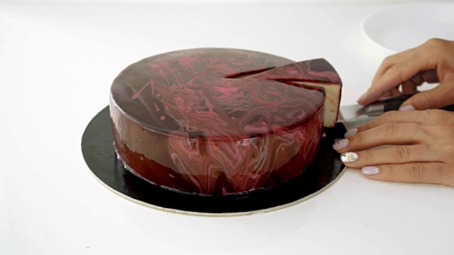 女性手切巧克力釉慕斯蛋糕的特写。视频下载
