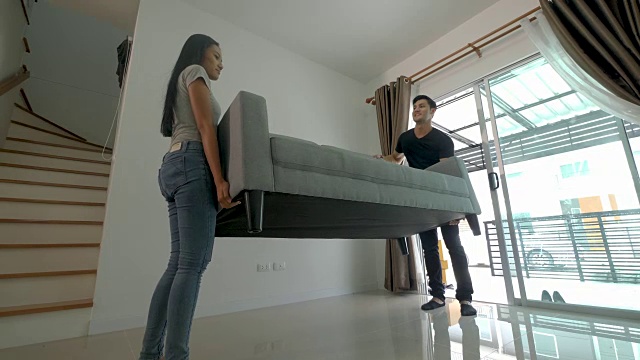 幸福的年轻亚洲夫妇移动沙发期间，他们搬进新房子视频素材