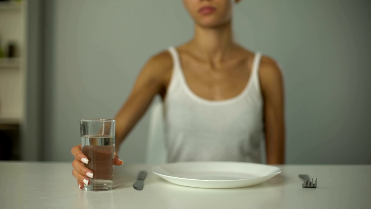 厌食症的女孩坐在空盘子前，喝水，严重节食视频下载