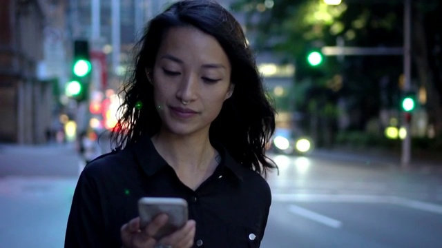 年轻女子拿着智能手机在夜里走在街上视频下载