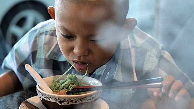 快乐的孩子在餐厅吃美味的面条。有视力障碍的亚洲男孩。左眼在脑部手术中是看不见的。恢复正常生活治疗效果。新生活视频下载