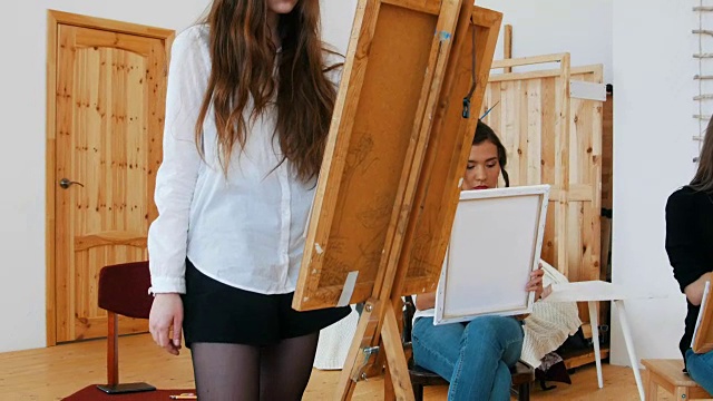 年轻漂亮的女人站在画架后面画画视频下载