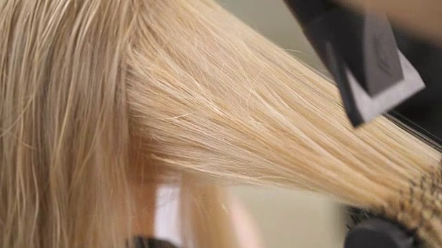 干燥的金发的特写。手用圆刷把一缕发丝，用吹风机吹几次直至发丝变长。视频素材