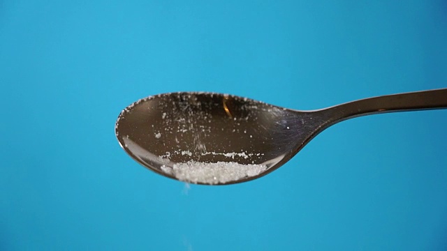 工作室图片一个金属勺子浇糖孤立在一个蓝色的背景在烹饪甜糖上瘾不健康的饮食超重和肥胖的概念视频素材