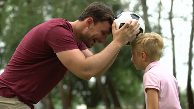 男孩和父亲在公园里踢足球，周末户外活动，积极的生活方式视频素材