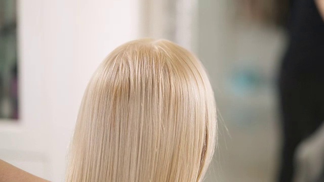 一个近距离的背影，金发的发梢刷一个通风口发刷。镜头从下往上移动，在头部上方定格。视频素材