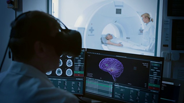 未来的概念:在医疗控制室，医生戴着虚拟现实头戴式耳机监测接受核磁共振或CT扫描的病人。电脑显示可能患有癌症的3D大脑模型。视频素材