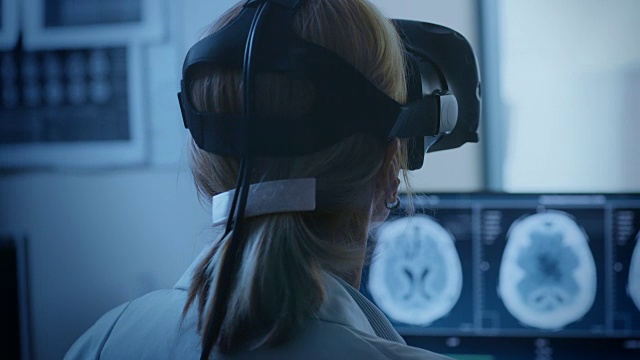 未来的概念:在医疗控制室女医生戴着虚拟现实耳机监测患者进行MRI或CT扫描程序。电脑显示脑部扫描。视频素材