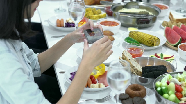一名中国妇女在吃饭时用智能手机和桌上的食物拍照。节日的概念、生日、新年快乐、圣诞快乐。4 k决议。视频下载