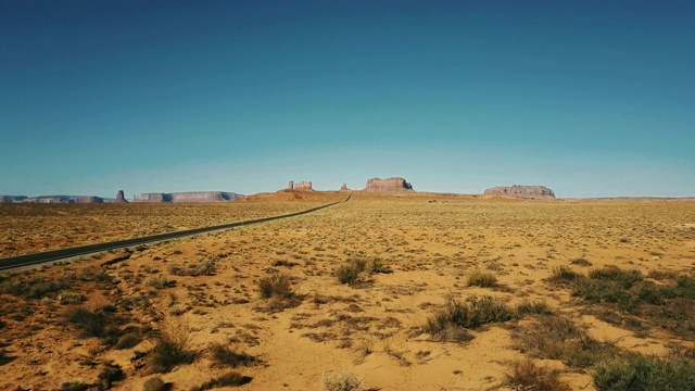 无人机在亚利桑那州和犹他州纪念碑谷附近干燥的美国砂岩沙漠上空低空飞行，晴朗晴朗的蓝天。视频素材