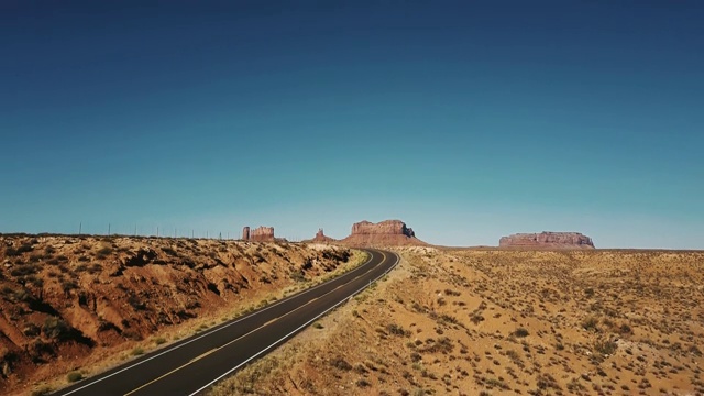 无人机在空旷的沙漠道路上升起，展示了美国阳光灿烂的纪念碑谷令人惊叹的无尽开阔空间。视频素材