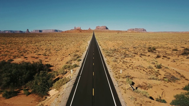 无人机向后飞行在纪念碑谷标志性的空砂岩沙漠道路，亚利桑那州与巨大的悬崖山脉。视频素材