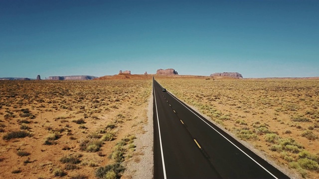 无人机跟随汽车在纪念碑谷的标志性美国沙漠高速公路上移动与巨大的悬崖山脉天际线。视频素材