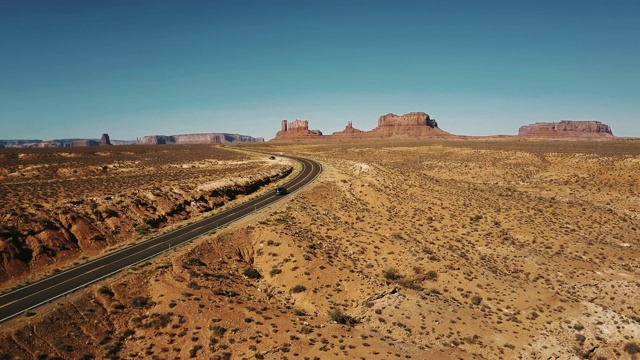 在美国阳光灿烂的纪念碑谷，汽车在沙漠高速公路上通过无人机摄像头，有令人惊叹的平坦山天际线。视频素材
