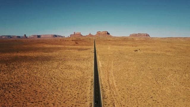 无人机向后飞行的空砂岩沙漠道路在纪念碑谷，亚利桑那州与平坦的山天际线。视频素材