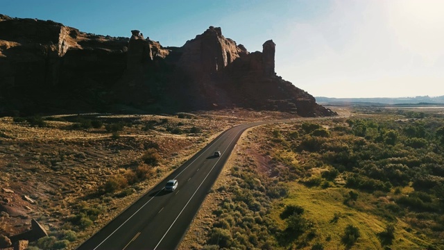无人机摄像头在日落美国沿着沙漠公路行驶的汽车靠近惊险的陡峭峡谷山脊。视频素材