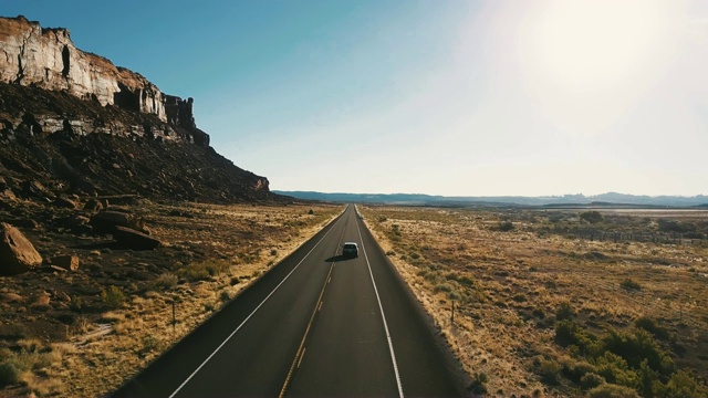 在美国，无人机跟随汽车在史诗般陡峭的峡谷山脊和惊人的沙漠天际线之间的高速公路上行驶。视频素材