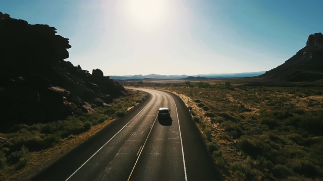 无人机摄像机跟随一辆小型货车在沙漠公路上左转，这条公路连接着令人叹为观止的开阔地带和山脉。视频购买