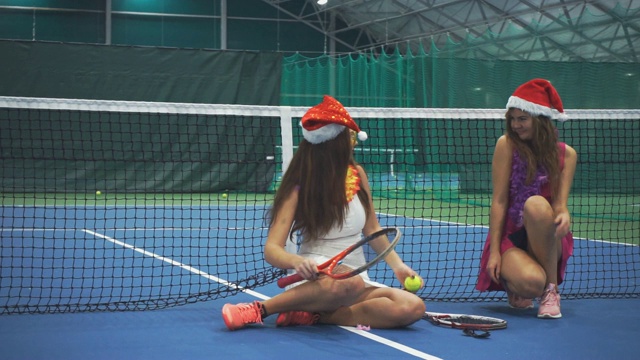 两个漂亮的女孩坐在网球场上，穿着新年的装饰品视频素材