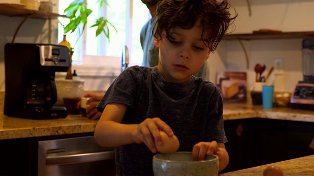 小男孩在厨房帮爸爸做早餐的时候打鸡蛋视频素材