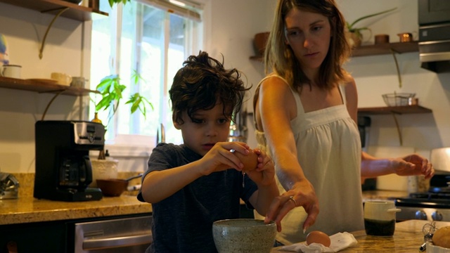 母亲看着儿子在厨房做早餐时把鸡蛋打到碗里视频素材