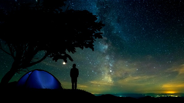 那个人站在山上靠近一棵露营的帐篷和树。时间流逝视频素材