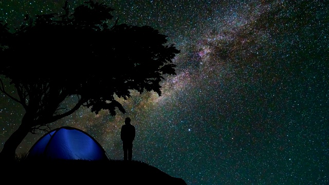 那个人站在山上，树映衬着星空。时间流逝视频素材
