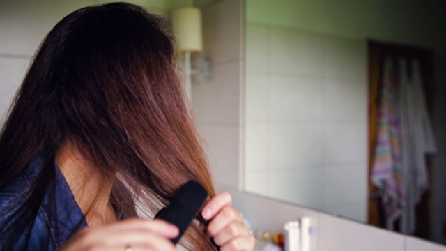 年轻女子在浴室里拉直头发。美丽的概念视频素材