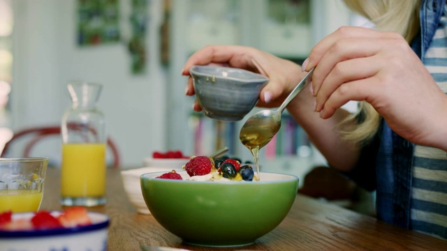 女子在格兰诺拉麦片中加入蓝莓和蜂蜜视频素材