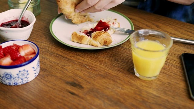 早餐桌上往牛角面包上抹黄油和果酱的女人视频素材