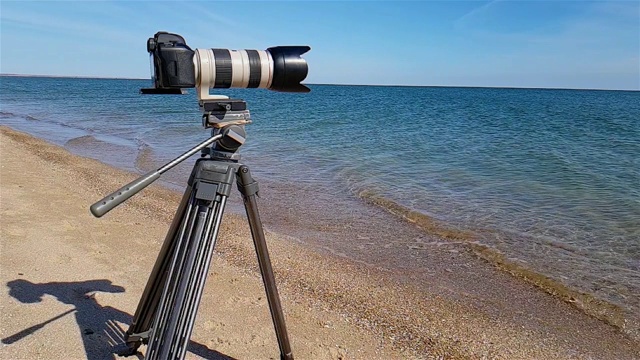 三脚架上的相机放在海边，相机拍摄海景，拍摄录像出售视频下载