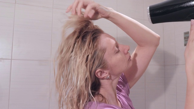 一个中年金发女人在浴室里用吹风机吹头发视频素材