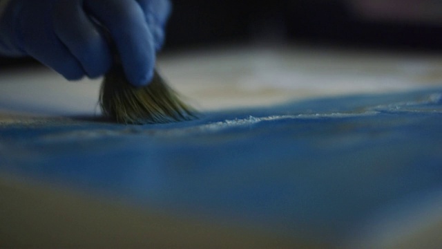 一位艺术家戴着防护手套在画布上涂抹油画的特写‭在一个室内艺术工作室视频素材