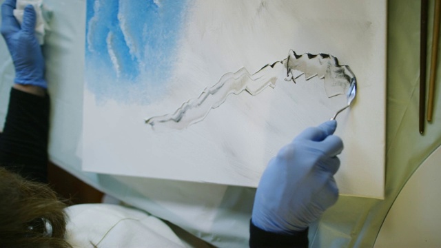 在室内艺术工作室，一位艺术家用调色板刀舀起油画颜料并将其涂在画布上视频素材
