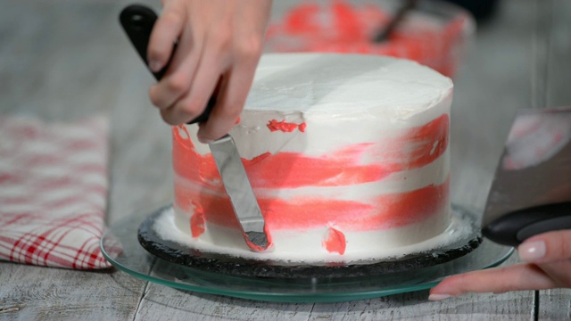 在面包店厨房的木制转盘上，糖果手在白色奶油蛋糕上涂抹粉色奶油。视频下载