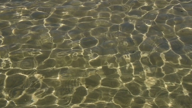 清澈的水面上有小波浪，动作缓慢，用美丽的阳光折射在水下的沙砾上荡漾视频素材