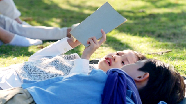 亚洲小女孩和小男孩躺在草地上看书视频素材