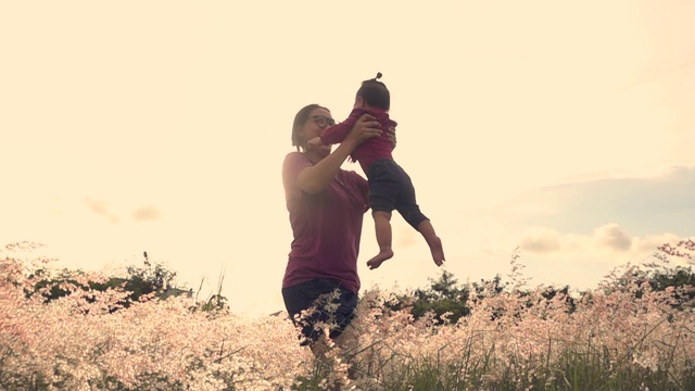 亚洲年轻的母亲和女儿在草地上日落。视频素材