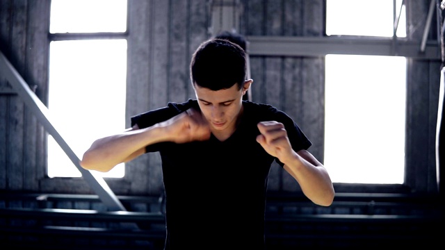 男拳击手伸展手臂，穿着黑色t恤。年轻运动员在拳击馆做热身运动，伸展手臂。背景上的Windows视频下载