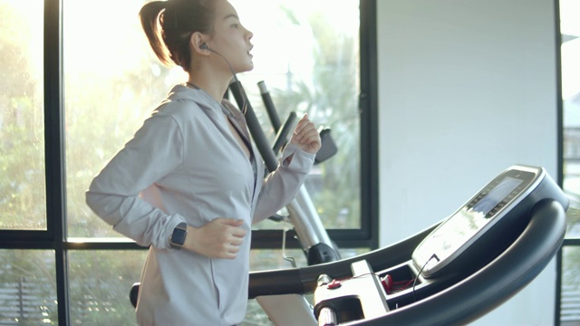 年轻女子在健身房的跑步机上锻炼和慢跑视频下载