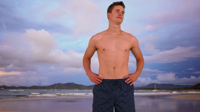 穿着短裤的白人站在沙滩上。年轻的白人单身汉欣赏着海滩的景色。4 k视频素材
