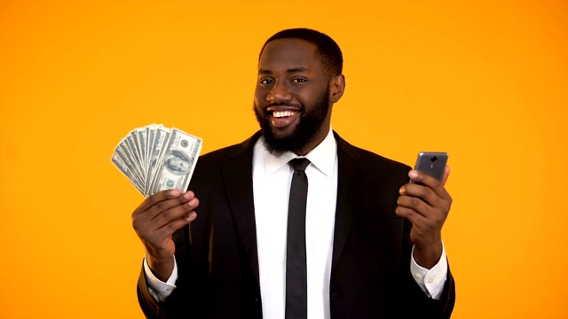 非裔美国男人穿着西装拿着手机和钞票，拿着现金视频下载