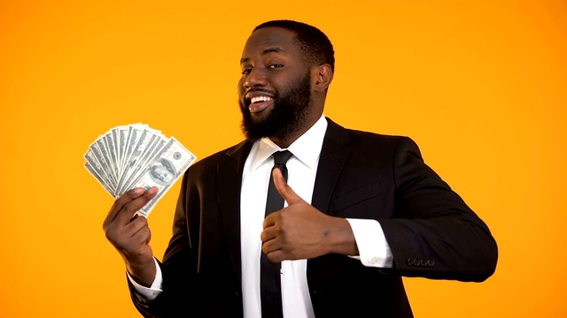 满意的黑人商人展示美元现金和竖起大拇指的手势，收入视频下载