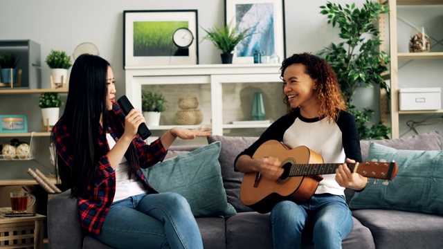 女性朋友在家里玩吉他，在电视遥控器上唱歌，一起在家享受休闲活动。音乐与文化概念。视频素材