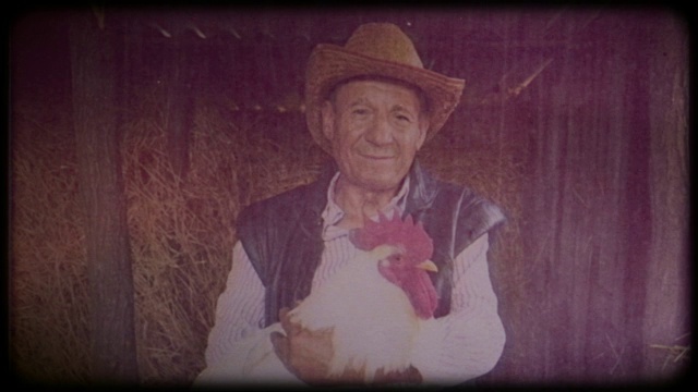 一个戴着草帽的农民手里拿着一只白色的大公鸡视频下载